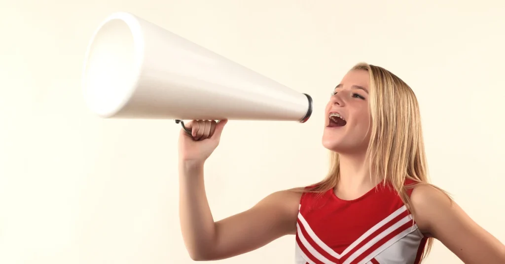 Cheerleader blonde en tenue rouge effectuant un scand dans un mégaphone de cheerleading blanc